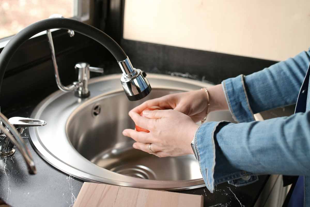 una donna sciacqua un frutto sotto l'acqua corrente in un lavello