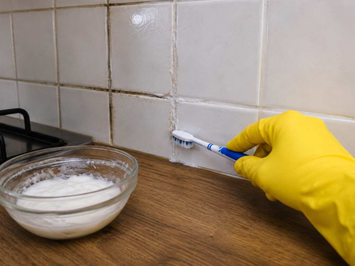 persona strofina miscela di bicarbonato sulle fughe delle piastrelle di una cucina