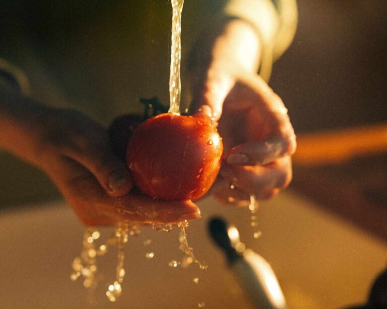 persona lava un pomodoro sotto il getto dell'acqua corrente